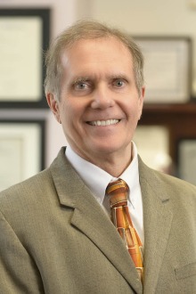 Portrait of Dr. Brian Erstad wearing a brown suit and orange tie